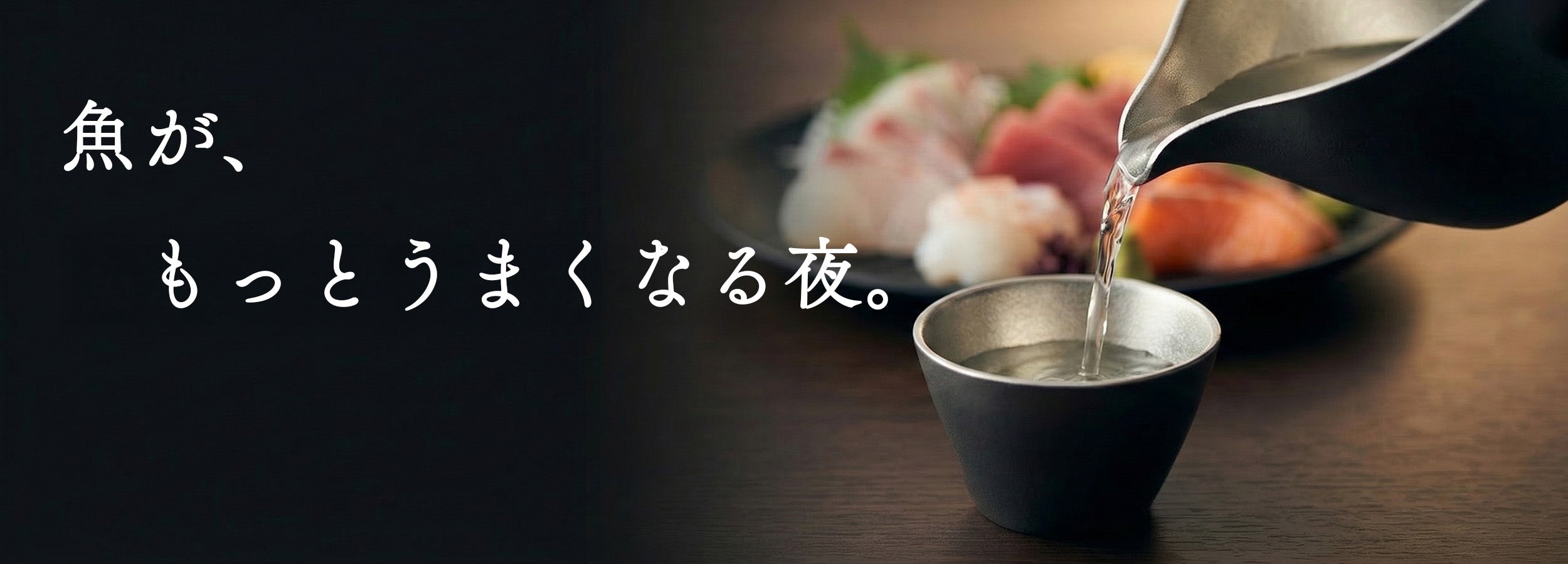 錫の片口から盃に日本酒を注いでいる瞬間。奥に刺身の盛り合わせ。「魚が、もっとうまくなる夜。」