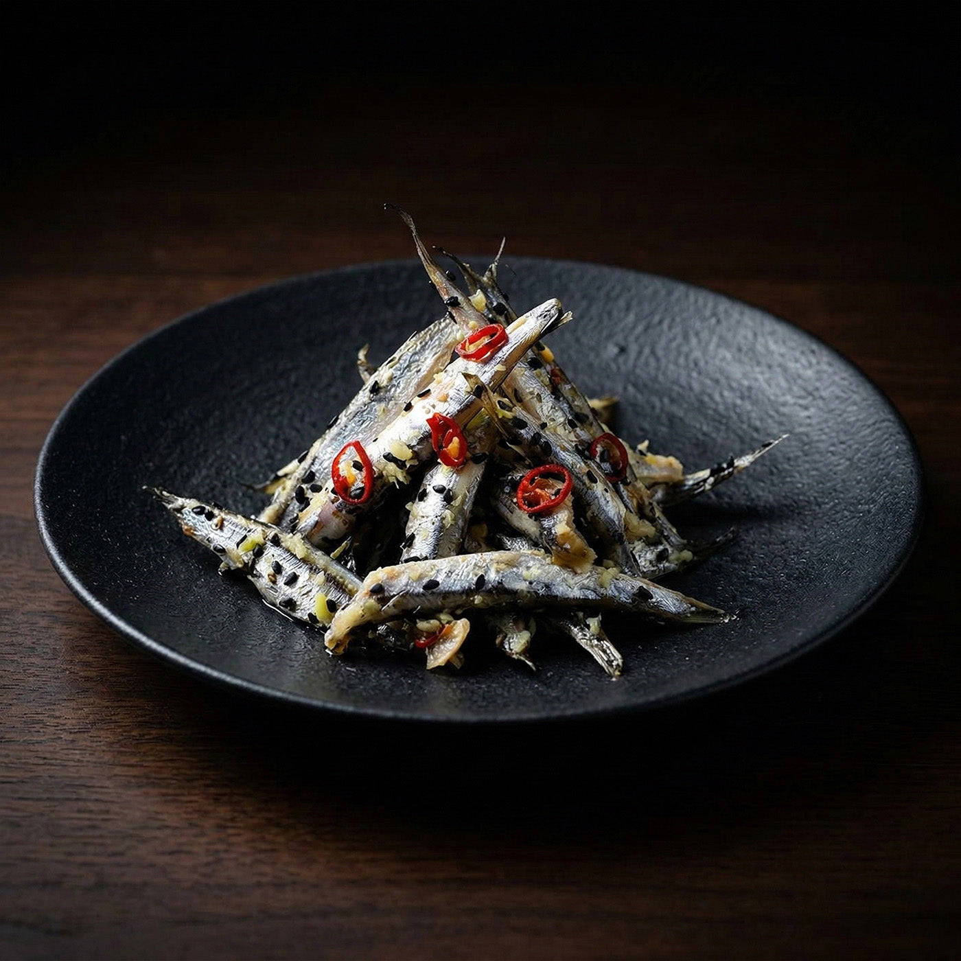 黒い皿に盛られた背黒イワシのごま漬け。黒ごまと赤唐辛子、針生姜